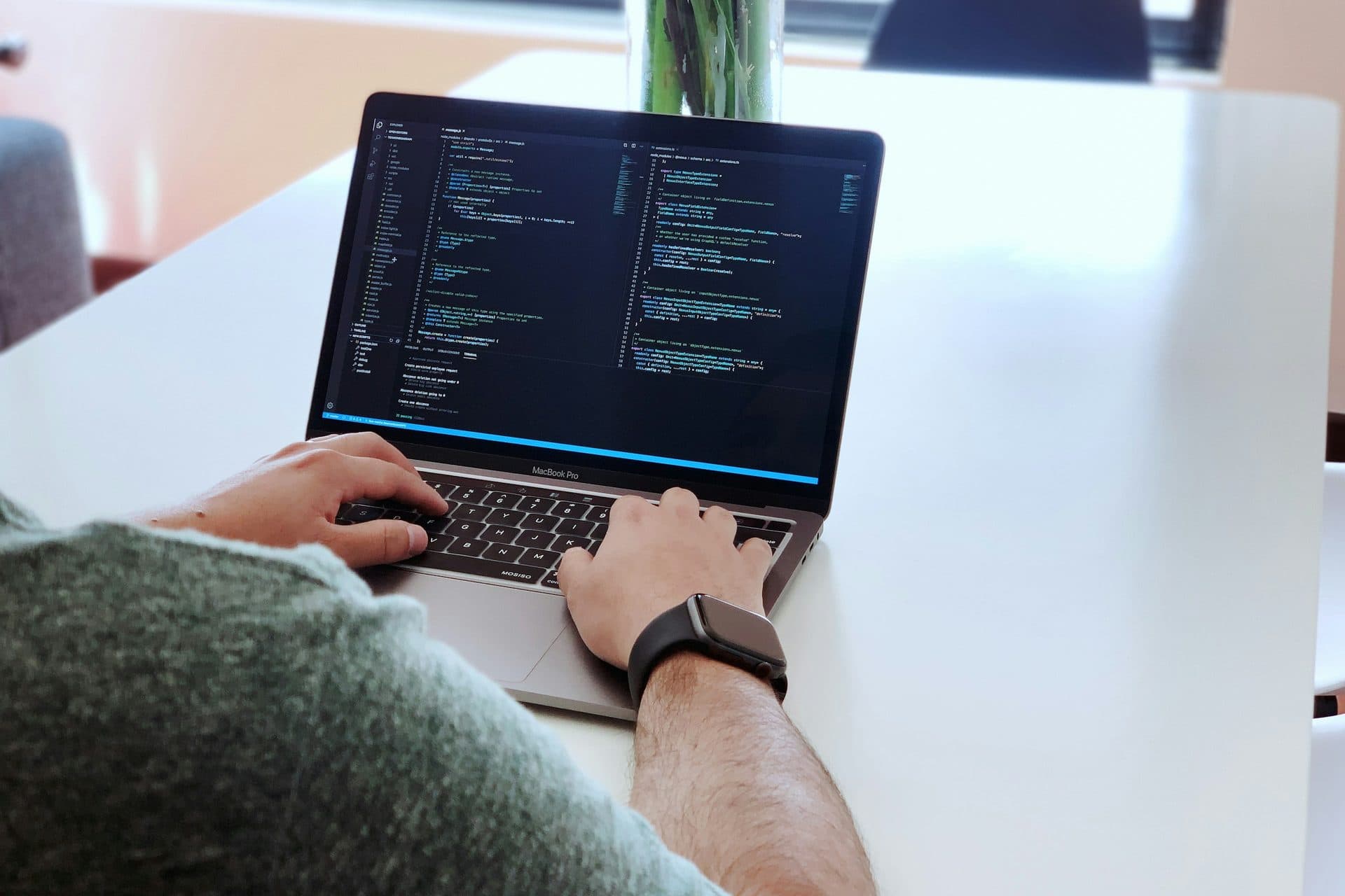 Iemand typt code op een laptop aan een witte tafel