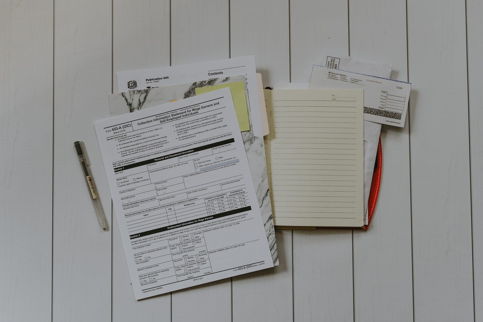 Ingevulde formulieren, een notitieboek en een pen op een witte houten tafel