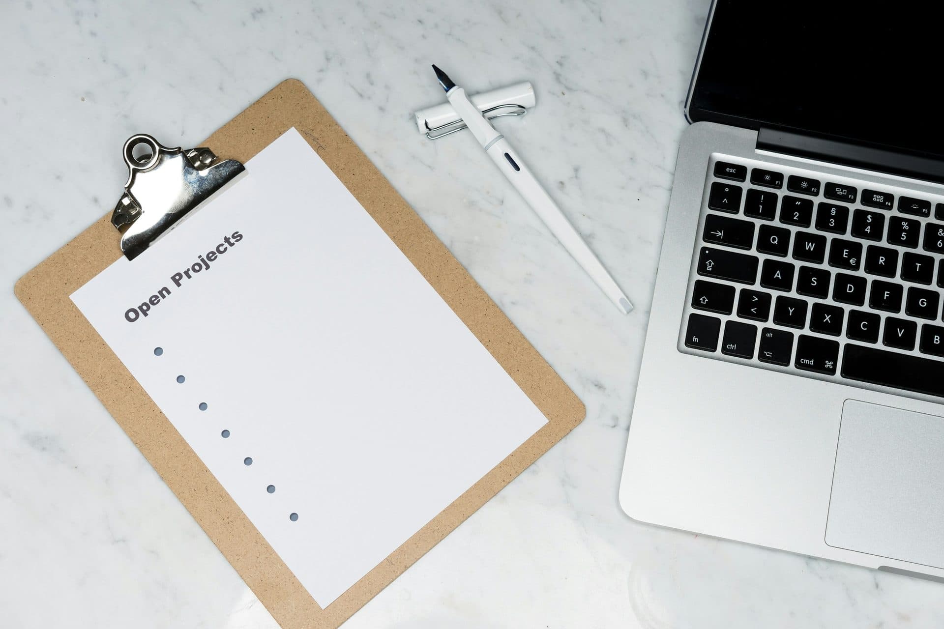 Klembord met een checklist naast een laptop en een pen op marmer