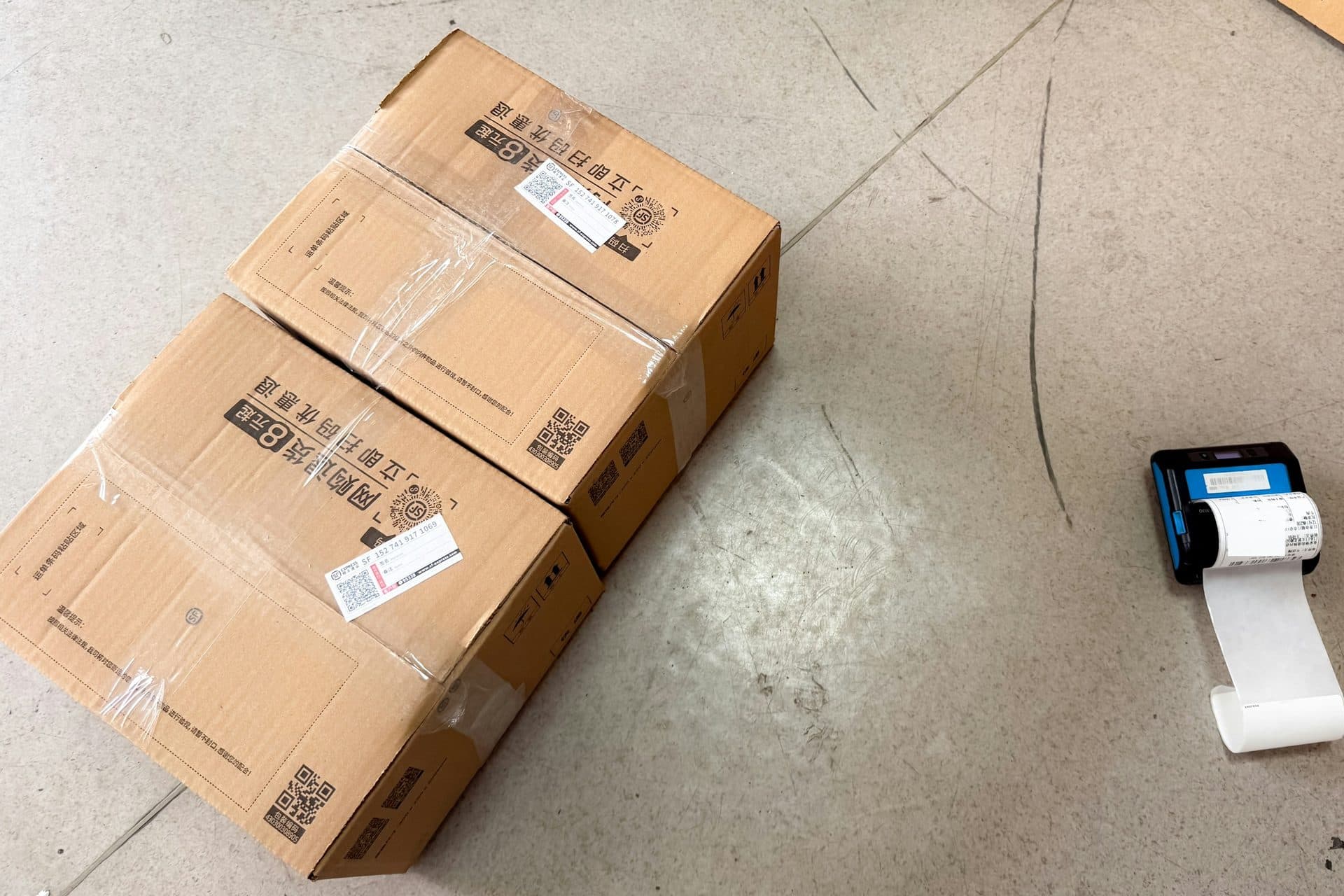 Kartonnen dozen met verzendlabels naast een kleine labelprinter op de vloer