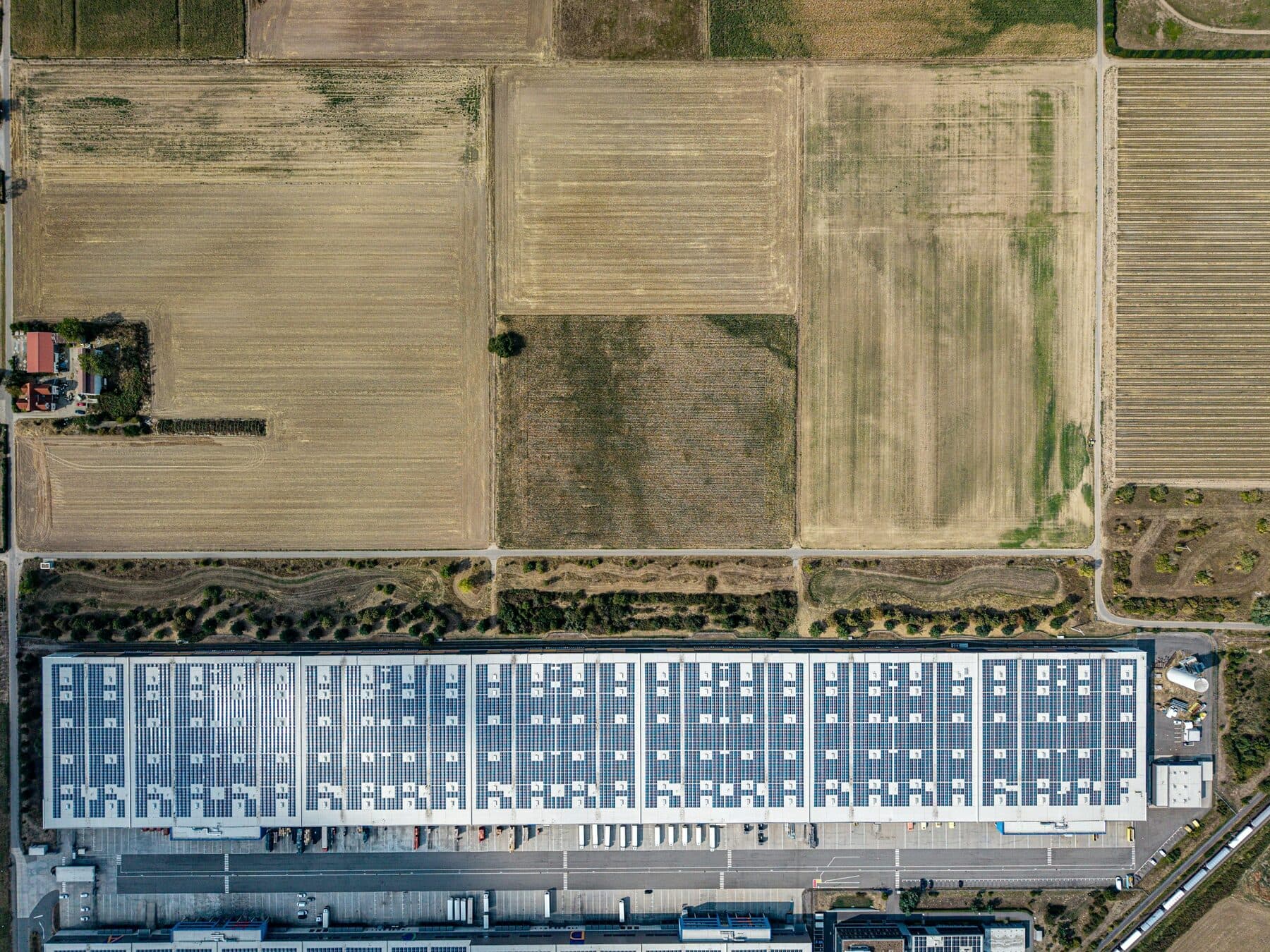 Factory with solar panels on the roof between fields, seen from above
